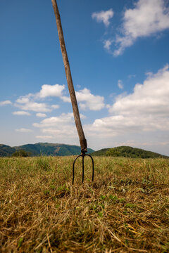 Pitchfork standing in dry grass field under blue sky
