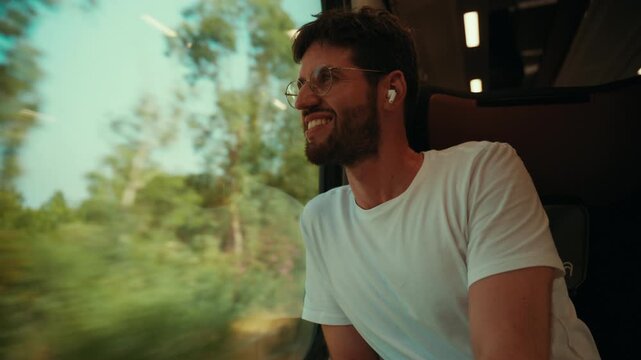 A smiling man wearing glasses looks out the window of a departing train