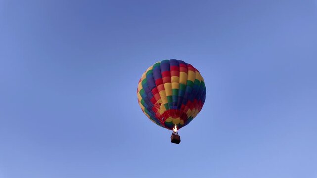 Colorful hot air balloon drifting in blue sky, peaceful daytime flight, recreational aviation sport, outdoor adventure, travel tourism concept.