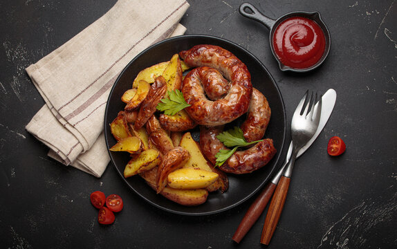Fried coiled meat sausages roasted potatoes ketchup grilled bbq black plate barbecue