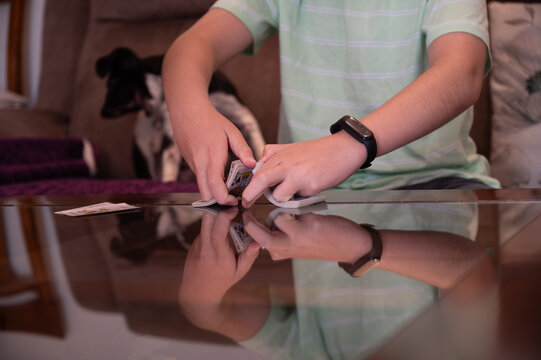Teenage boy shuffling a deck of playing cards on a glass table at home while preparing for a card game with copy space