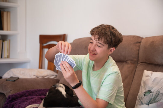 Smiling teenage boy holding a winning hand of playing cards while enjoying a family card game at home with his pet dog nearby
