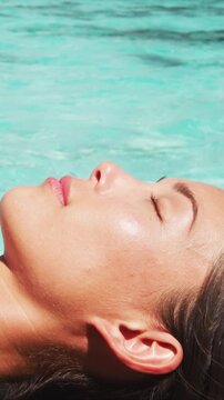 Skin care beauty and sun protection woman sun bathing by perfect water ocean beach. Close up of face. Multicultural mixed race model. Raw unedited vertical video of real woman model without any makeup