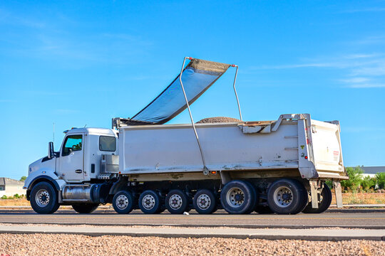 Dump truck hauling aggregate with a retractable mesh tarp system on a roadway, illustrating commercial trucking, bulk material transport, construction logistics, and freight operations