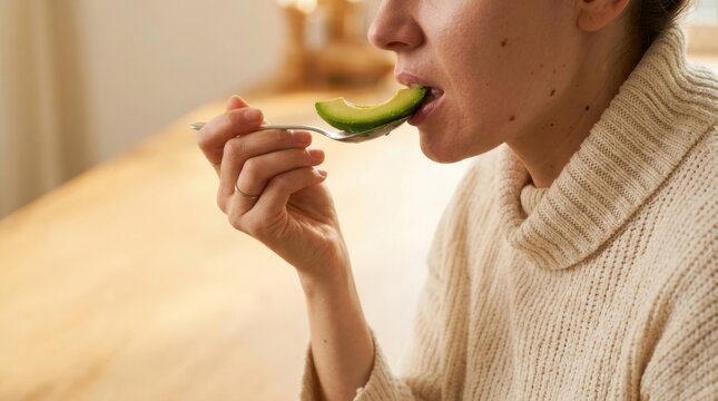 Woman eating a slice of fresh avocado from a spoon enjoying a healthy snack Healthy lifestyle