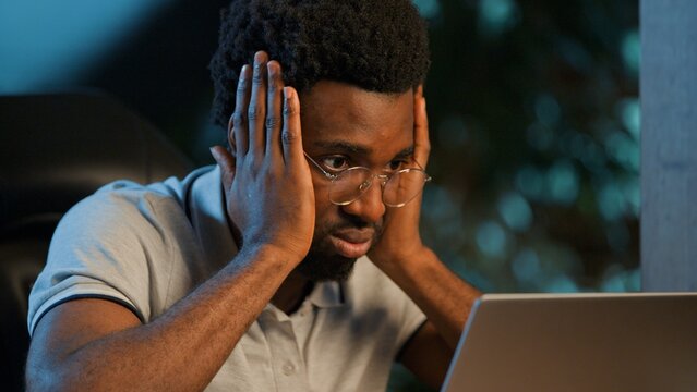 Tired stressed African American business man holding head looking at laptop at night office ethnic male businessman guy executive professional feeling headache overworked with computer fail at evening