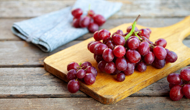 Red grapes cluster on cutting board. Rustic wooden background. Close up.