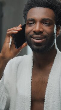Cheerful African American man friendly talking mobile phone looking at mirror reflection at home bathroom carefree ethnic guy talk smartphone enjoying conversation at morning hygiene beauty routine