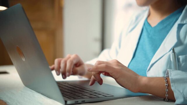 Close-up of an anonymous young female nurse's hands typing on a laptop, representing healthcare technology, clinical documentation, professional work, and digital medical tasks.
