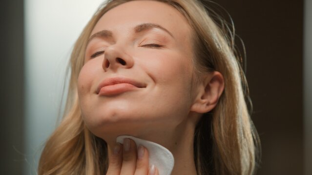 Smiling cheerful Caucasian woman wiping sensual skin with cotton pad cosmetology treatment carefree female smile wiping face with toner cleanser remover dermatology procedure beauty routine in evening