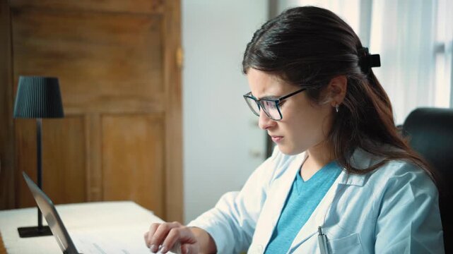 Young Hispanic female medical secretary experiencing significant wrist pain from tendonitis while working in her medical office, representing workplace discomfort, repetitive strain, ergonomics, and o