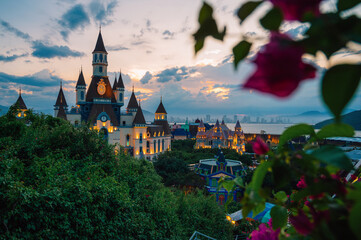 Illuminated castle-inspired of Vinpearl in VinWonders theme park overlook a scenic bay at dusk, creating a magical waterfront cityscape with mountains, dramatic clouds, and evening lights. © olinchuk
