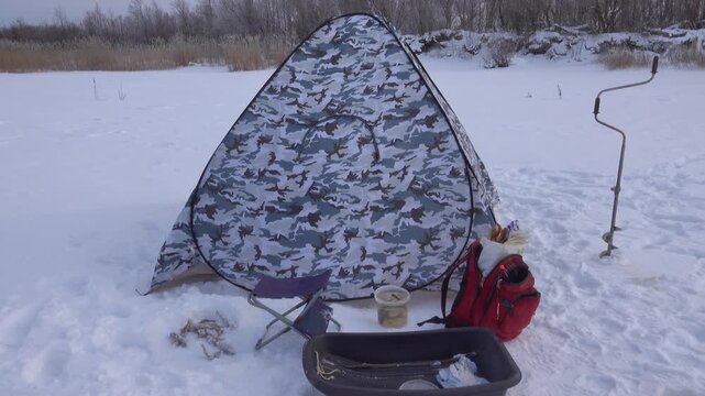 Winter (ice) fishing. A special fishing tent on ice, with no bottom and holes drilled inside. Fishing equiptent, plastic sledge and ice drill. Bunch of roach near the hole