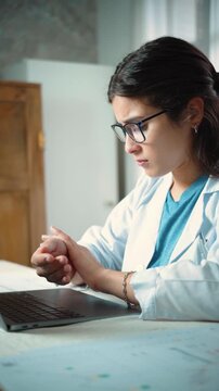 Young Hispanic female nurse experiencing tendonitis from typing on her laptop, representing repetitive strain, workplace discomfort, healthcare work, and occupational health.
