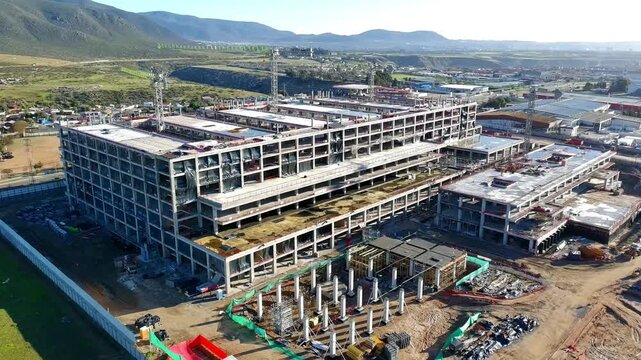 Aerial view of hospital construction site with cranes and dirt lot foreground Keywords extra: dirt lot, cranes, construction equipment, exposed structure, oblique angle