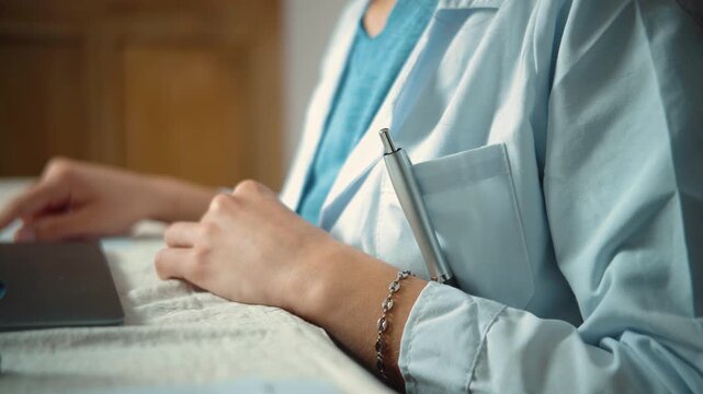 Detailed shot of a pen tucked into a young female doctor's white coat, followed by her taking it out to write, representing medical work, clinical routines, and professional healthcare practice.
