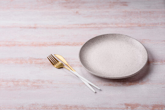 An empty round ceramic plate on a dark, textured white background. An empty round plate