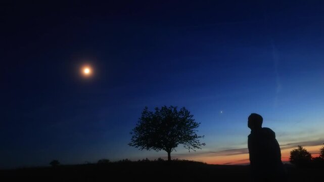 Silhouette of a person in nature observing night sky, Moon, stars and planets from a remote location.
