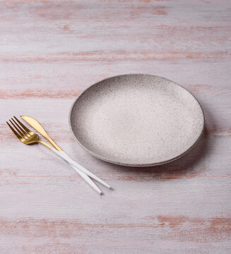 An empty round ceramic plate on a dark, textured white background. An empty round plate
