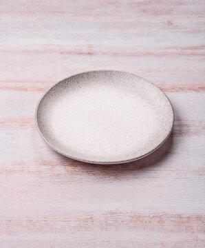 An empty round ceramic plate on a dark, textured white background. An empty round plate