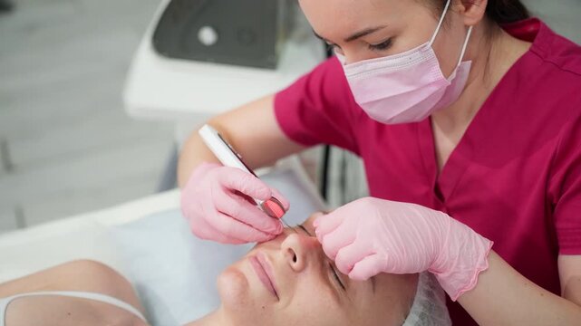 Skincare specialist in a pink uniform and medical mask performing an ultrasonic peeling procedure on a woman's face, providing professional cosmetic care and rejuvenation in a spa clinic