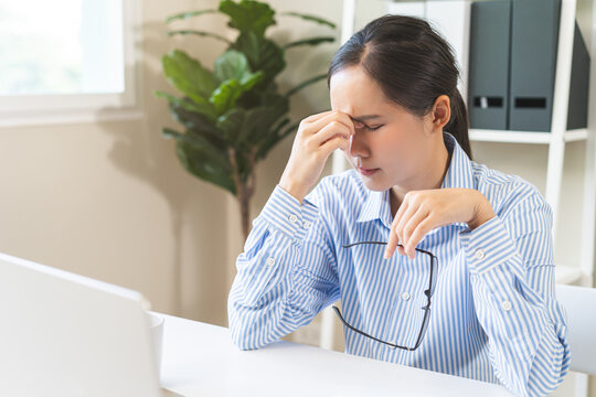 Eye problem concept, fatigue asian young woman tired eyes, irritated rubbing nose, relief vision pain after work on laptop computer, eye strain, hand holding glasses, suffer migraine, bad blurry.