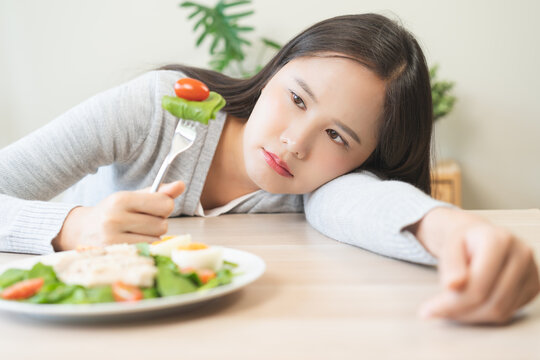 Diet in bored face, unhappy beautiful asian young woman, girl on dieting, holding fork at tomato on salad plate, dislike or tired with eat fresh vegetables. Nutrition of clean, healthy food good taste