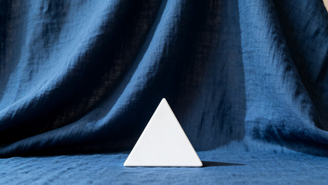 equilateral. Single white equilateral triangle object on deep blue linen, calm still life for editorial concept, lifestyle magazines.