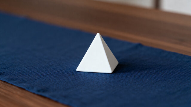 equilateral. Single white equilateral triangle object on deep blue linen, calm still life for editorial concept, lifestyle magazines.