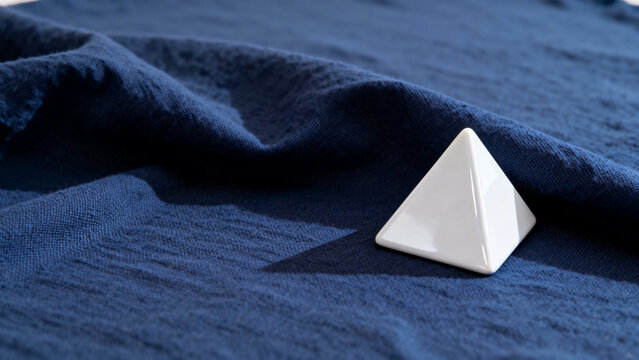 equilateral. Single white equilateral triangle object on deep blue linen, calm still life for editorial concept, lifestyle magazines.
