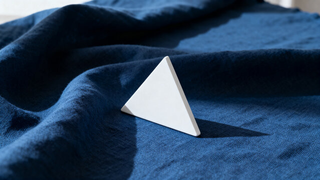 equilateral. Single white equilateral triangle object on deep blue linen, calm still life for editorial concept, lifestyle magazines.