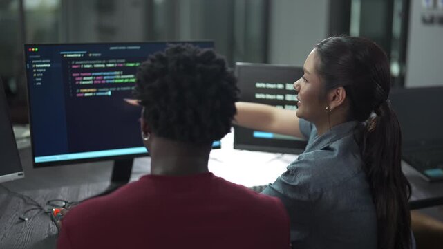 Over-the-shoulder shot of two diverse programmers working together on a coding project in a modern office.