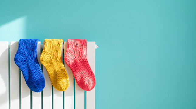 Colorful socks drying on a heater against a blue wall with copy space