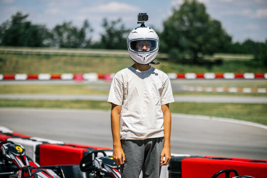 Teenager in racing gear and helmet with camera looking at lens before go-karting