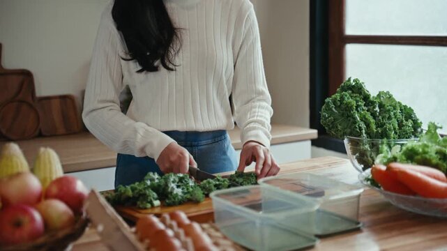 Close-up of a young woman chopping fresh kale on a wooden board. Healthy meal preparation with organic vegetables for a balanced diet
