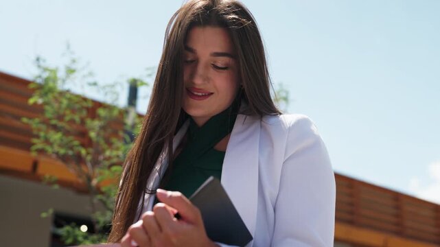 Beautiful business woman sitting on wooden bench and writing in notebook, closeup shot