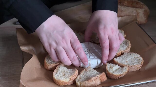 Placing sliced brie cheese on baking tray with bread during homemade food preparation in home kitchen, arranging soft cheese by hand before cooking