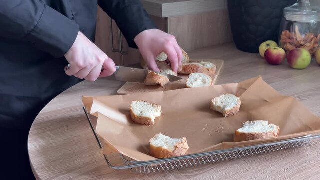 Cutting bread slices in half and placing them on baking tray during homemade food preparation in home kitchen, preparing bread for cooking with human hands