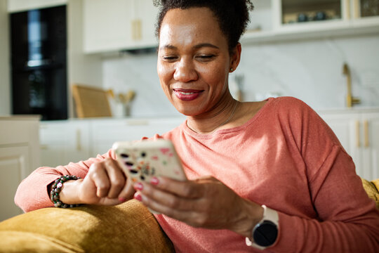 Smiling woman using smartphone on couch at home