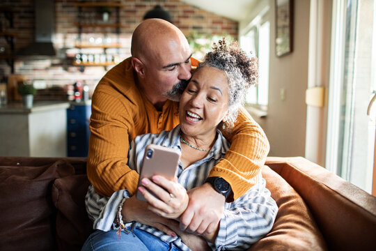 Affectionate mature couple taking selfie on couch at home