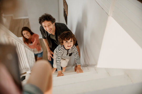 Parents guide young child up stairs at home