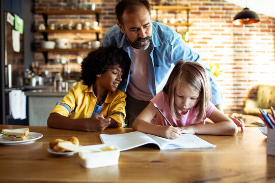 Father helping children with homework at the kitchen table at home