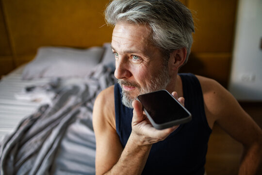 Mature man recording voice message in bedroom