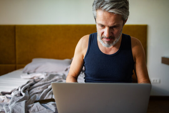 Middle-aged man using laptop in bed at home