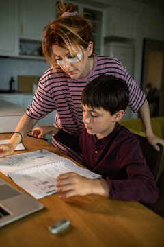 Mother helping son with homework at kitchen table at home