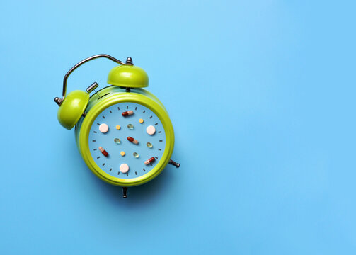 Green alarm clock with pills on blue background, medication reminder and healthcare schedule concept