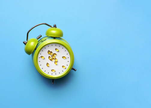 Green alarm clock with pills on blue background, medication reminder and healthcare schedule concept