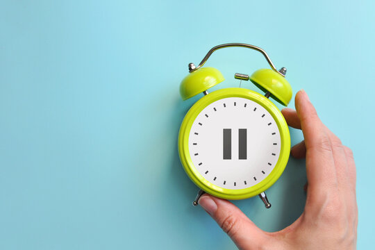 Hand holding alarm clock with pause icon, take a break concept