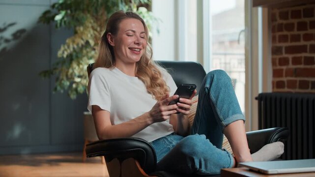 Caucasian woman using mobile phone app smiling laughing watching humorous video at home office middle-aged female browsing social media enjoy scrolling smartphone funny content smile laugh relaxing