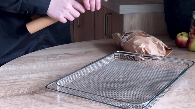 Lining baking tray with parchment paper from roll during food preparation in home kitchen, unrolling, tearing and adjusting baking paper with human hands